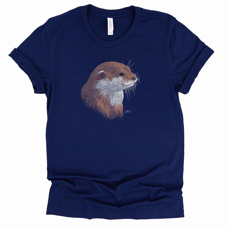 May include: A navy blue t-shirt with a brown and white otter illustration on the front. The otter is looking to the right and has a small signature in the bottom right corner.