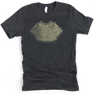May include: Dark gray t-shirt featuring a detailed illustration of a reptile's head with red eyes. The artwork is centered on the shirt and has a textured appearance. The shirt is made of a soft material.