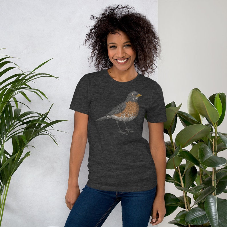 May include: A dark heather grey t-shirt with a robin illustration. The robin is brown, grey, and white with a yellow beak.