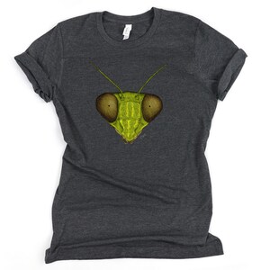 May include: A dark heather grey t-shirt with a green praying mantis face graphic printed on the front.