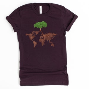 Puede incluir: Una camiseta de color morado oscuro con un &aacute;rbol verde que crece fuera del mundo, con ra&iacute;ces marrones.