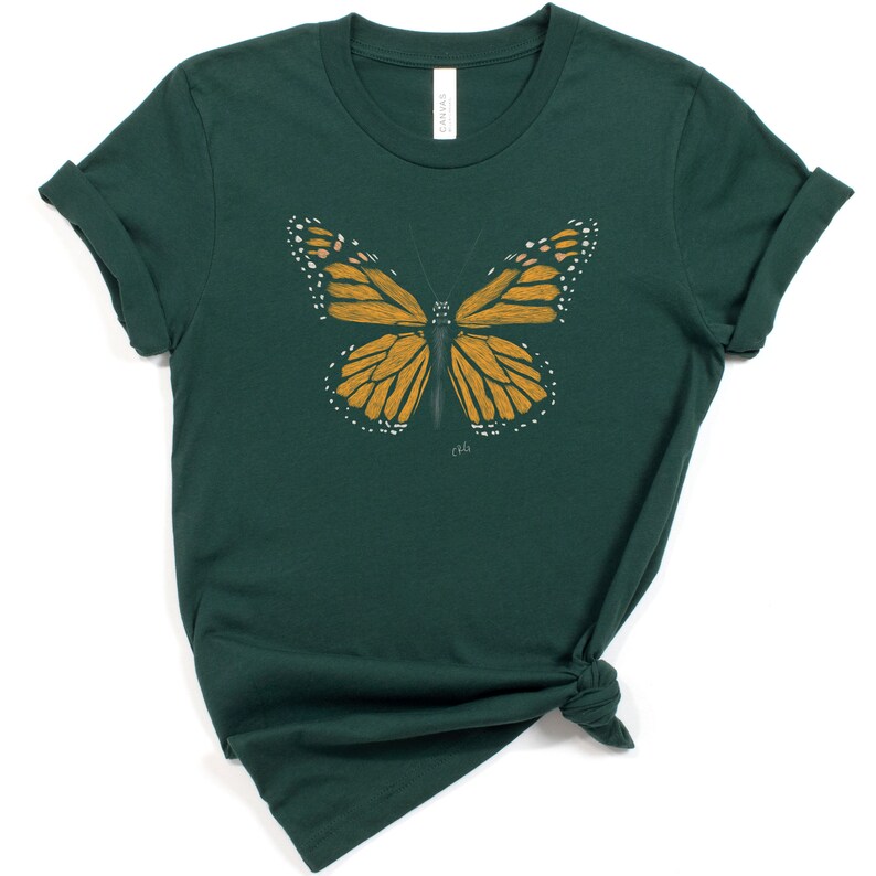 May include: A dark green t-shirt with a yellow and black butterfly graphic. The butterfly is centered on the shirt and has a white outline.