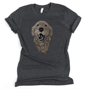 May include: A dark heather grey t-shirt with a detailed illustration of a golden retriever dog's head. The dog is looking directly at the viewer with its mouth open and tongue slightly out.