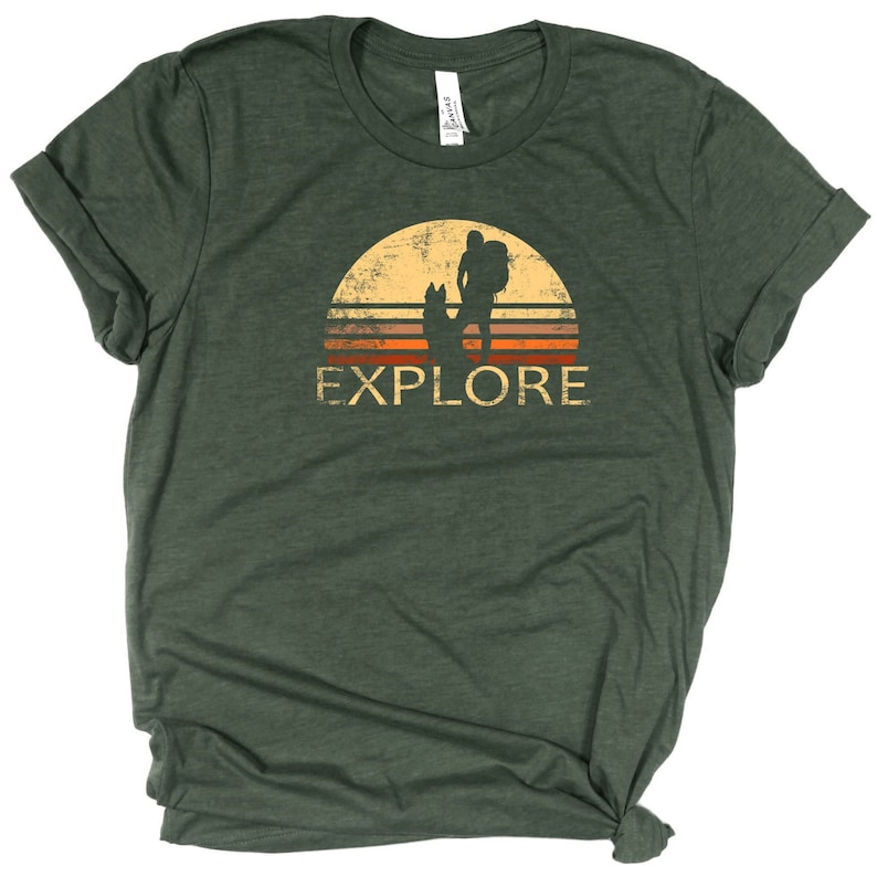 May include: Green t-shirt with a distressed graphic of a hiker with a dog silhouetted against a sunset. The word "EXPLORE" is printed below the image in a vintage style.