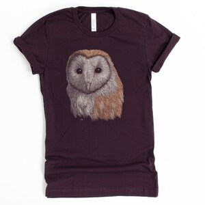 K&ouml;nnte beinhalten: Ein dunkelviolettes T-Shirt mit einer Illustration einer wei&szlig;en und braunen Scheune Eule auf der Vorderseite.