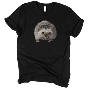 Peut inclure: Un t-shirt noir avec un imprim&eacute; d'un h&eacute;risson souriant. Le h&eacute;risson est brun et gris avec un ventre blanc et des yeux noirs.