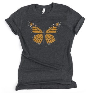 May include: A dark grey t-shirt with a graphic of a monarch butterfly in shades of orange and black.