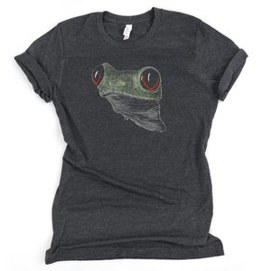 May include: A dark heather grey t-shirt with a white outline drawing of a frog with red eyes. The frog is facing the viewer.