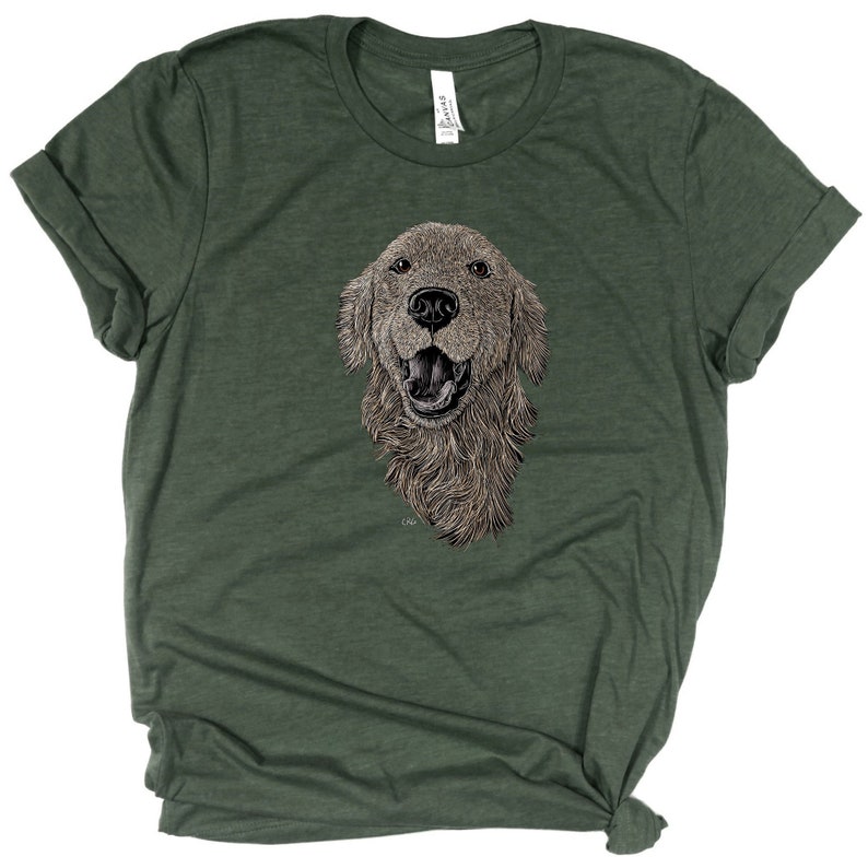 May include: A green t-shirt with a detailed illustration of a golden retriever dog's head. The dog is looking directly at the viewer with its mouth open and tongue slightly out. The illustration is in black and white with a slight brown tint.