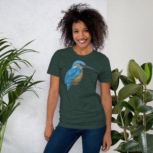 May include: A woman wearing a dark green t-shirt with a blue and brown kingfisher bird graphic. The bird is facing left and has a long, thin beak.