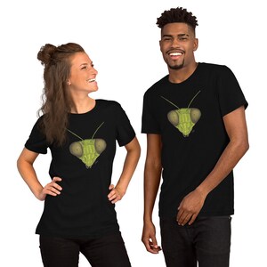May include: Two people wearing black t-shirts with a green praying mantis face graphic printed on the front.