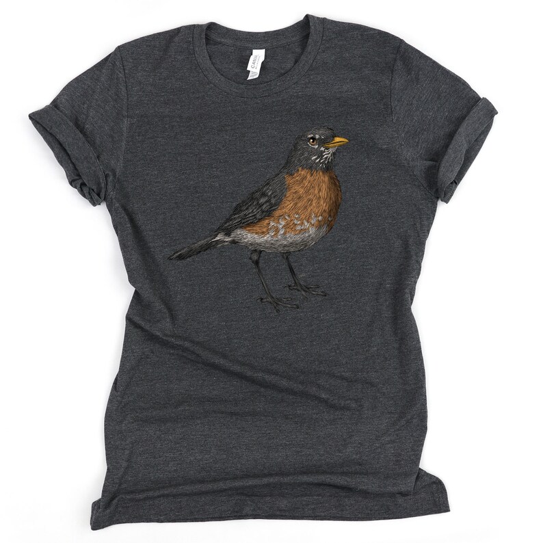 May include: A dark heather grey t-shirt with a robin illustration in the center. The robin is brown, orange, and black with a yellow beak.