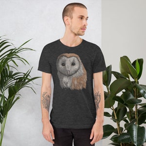 K&ouml;nnte beinhalten: Ein dunkelgraues T-Shirt mit einem realistischen Motiv einer Schleiereule auf der Vorderseite. Die Eule hat braune und wei&szlig;e Federn und gro&szlig;e, gelbe Augen.
