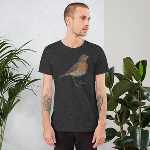 May include: A dark heather grey t-shirt with a graphic of a robin bird. The bird is depicted in a realistic style with brown, grey, and white feathers.