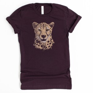 May include: A dark purple t-shirt with a cheetah face graphic printed on the front. The cheetah is depicted in a realistic style with brown and tan fur.