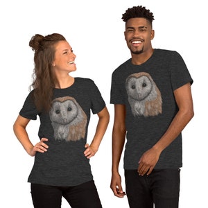 K&ouml;nnte beinhalten: Zwei Personen tragen dunkelgraue T-Shirts mit einem wei&szlig;en Scheunen-Eulen-Motiv auf der Vorderseite. Die Eule hat braune und wei&szlig;e Federn.