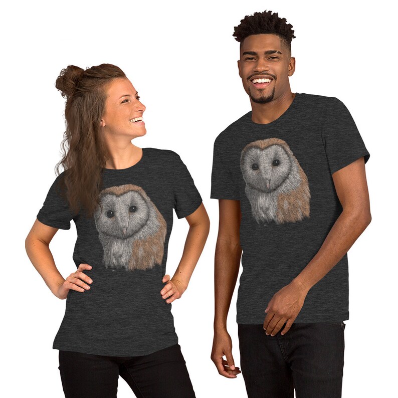 K&ouml;nnte beinhalten: Zwei Personen tragen dunkelgraue T-Shirts mit einem wei&szlig;en Scheunen-Eulen-Motiv auf der Vorderseite. Die Eule hat braune und wei&szlig;e Federn.