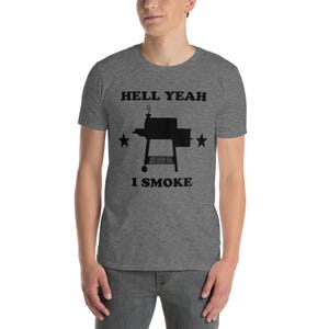 Peut inclure: T-shirt gris chiné avec l'inscription noire « HELL YEAH I SMOKE », un dessin de fumoir et deux étoiles. Le t-shirt est à manches courtes.