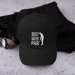 May include: Black baseball cap with the text "BEST DAD BY PAR" in white, along with a white silhouette of a golfer. The cap is a classic style, suitable for golf enthusiasts.