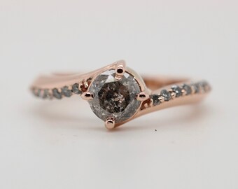 May include: A rose gold engagement ring with a grey diamond center stone and a band of smaller grey diamonds.
