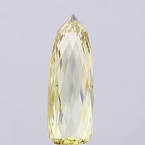 May include: A faceted, elongated crystal with a pointed top. The crystal is a pale yellow color and has a geometric pattern of diamond-shaped facets. The crystal is standing upright against a plain white background.