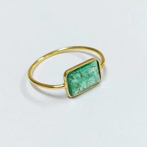 May include: A gold ring with a rectangular emerald green gemstone.
