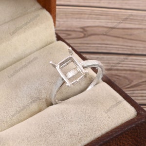 May include: A silver ring with a square-shaped setting for a gemstone. The ring is in a velvet-lined box.