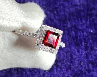 May include: A silver ring with a square red gemstone surrounded by smaller white gemstones.