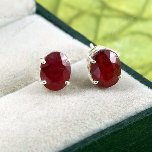 Puede incluir: Un par de pendientes de plata con piedras preciosas de rubí rojo de forma ovalada.