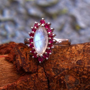 May include: A silver ring with a large, oval-shaped moonstone set in a halo of small, red ruby stones.