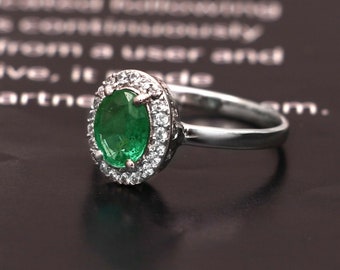 May include: A silver ring featuring a large oval emerald gemstone surrounded by smaller clear gemstones.
