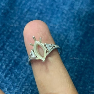 May include: A silver-toned ring setting featuring a central marquise-shaped prong mount designed for a gemstone, flanked by two small triangular clear stones on each side of the band. The metal has a polished finish and a four-prong setting style.