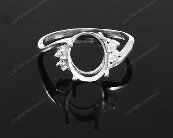 May include: A silver-toned ring setting featuring an oval-shaped center mount designed for a gemstone. The band includes small, clear, faceted stones set on either side of the central oval. The text LaziGemsnJewels is visible on the image.