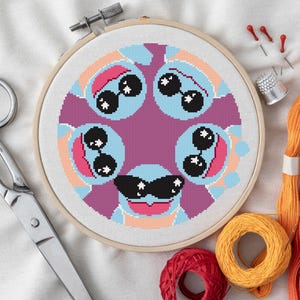 May include: A cross-stitch embroidery in a wooden hoop features a repeating pattern of cartoon characters wearing sunglasses. The design uses shades of blue, pink, and purple. Scissors, thread, and needles are arranged around the hoop.