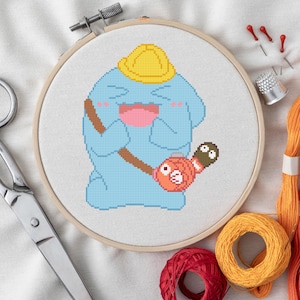 May include: Cross-stitch embroidery hoop featuring a blue cartoon character wearing a yellow hard hat and holding a brown and orange object. The image includes scissors, thread, needles, and a thimble.