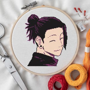 Könnte beinhalten: Ein Kreuzstich-Porträt einer Figur mit dunkelviolettem Haar in einem hölzernen Stickrahmen. Das Bild ist von Stickzubehör umgeben, darunter Schere, Faden und Nadeln.