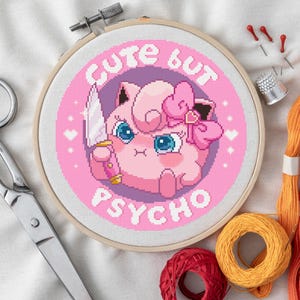Puede incluir: Un bastidor de bordado de punto de cruz con un personaje de dibujos animados rosa sosteniendo un cuchillo, con las palabras "Cute but Psycho". La imagen incluye tijeras, hilo, agujas y un dedal, lo que sugiere un tema de manualidades.