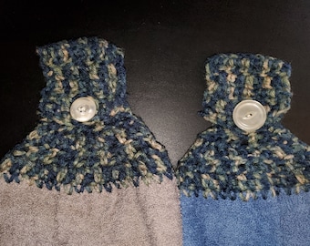 May include: Two crocheted dish towels with a blue, green, and beige pattern. Each towel has a white button sewn on the top.