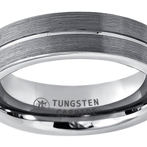Puede incluir: Un anillo de carburo de tungsteno plateado cepillado con una sola línea fina de plata pulida alrededor de la banda. El anillo está grabado con "TUNGSTEN CARBIDE" y un logotipo de corona.