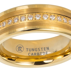 Puede incluir: Un anillo de carburo de tungsteno dorado con acabado cepillado y una fila de piedras de circonita cúbica transparentes alrededor de la banda. El anillo está grabado con "TUNGSTEN CARBIDE".