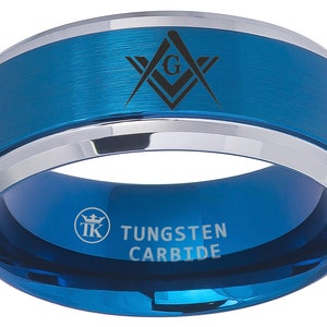 Op de afbeelding: Een blauwe ring van wolframcarbide met een zilveren band en een vrijmetselaars symbool gegraveerd op de bovenkant. De ring is gegraveerd met "TUNGSTEN CARBIDE" en een logo.