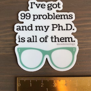 May include: White sticker with black text that reads "I've got 99 problems and my Ph.D. is all of them."  The text is followed by a pair of green glasses with black dots on the sides.