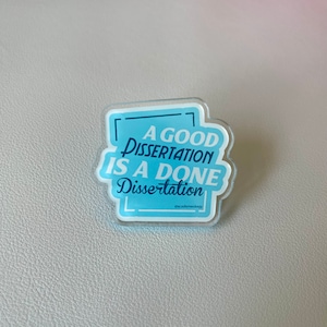 May include: A blue and white acrylic pin with the text "A good dissertation is a done dissertation" and the hashtag "#academecology".