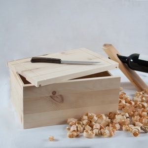 Puede incluir: Una caja de madera con tapa abatible, un pequeño cuchillo en la parte superior de la tapa y virutas de madera esparcidas alrededor de la caja.