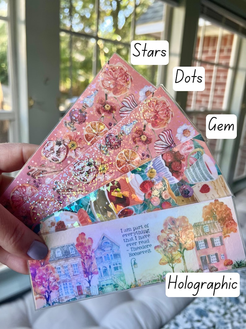 May include: A set of four decorative bookmarks with different designs. The bookmarks are made of clear plastic with a holographic finish. The designs include stars, dots, gems, and a house with trees. The quote "I am part of everything that I have ever read - Theodore Roosevelt" is printed on the house bookmark.