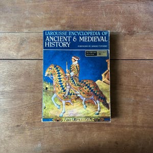 May include: A hardcover book titled Larousse Encyclopedia of Ancient & Medieval History with a blue and gold cover illustration of a knight on horseback. The cover features the text Foreword by Arnold Toynbee and Ano Dm Mcccxxviii.