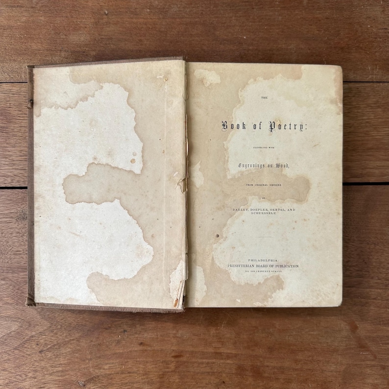 May include: An open antique book titled "The Book of Poetry" with visible water stains on the pages. The book's cover is a faded brown, and the pages are off-white with black text. The book is lying on a wooden surface.
