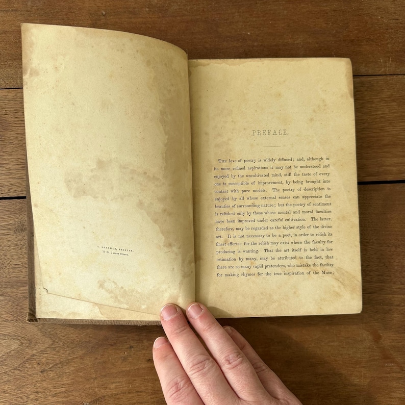 May include: Open antique book with aged, yellowed pages. The text on the right page reads "PREFACE." The book is open, revealing printed text. The book's cover is visible on the left side. The book is on a wooden surface.