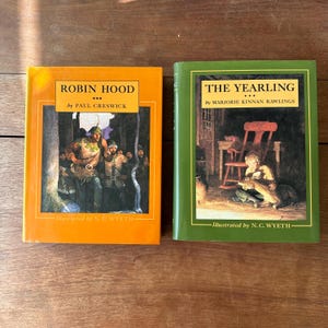 May include: Two vintage hardcover books: "Robin Hood" in orange and "The Yearling" in green. Both books feature illustrations by N.C. Wyeth. The "Robin Hood" book has a forest scene, while "The Yearling" shows a child with an animal.
