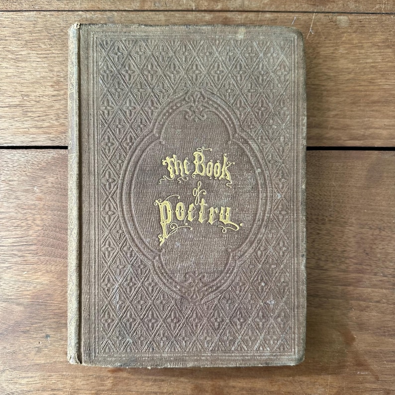 May include: An antique book titled "The Book of Poetry" with gold lettering on the cover. The cover is a muted brown color with a diamond pattern and an oval design around the title. The book appears to be well-worn.